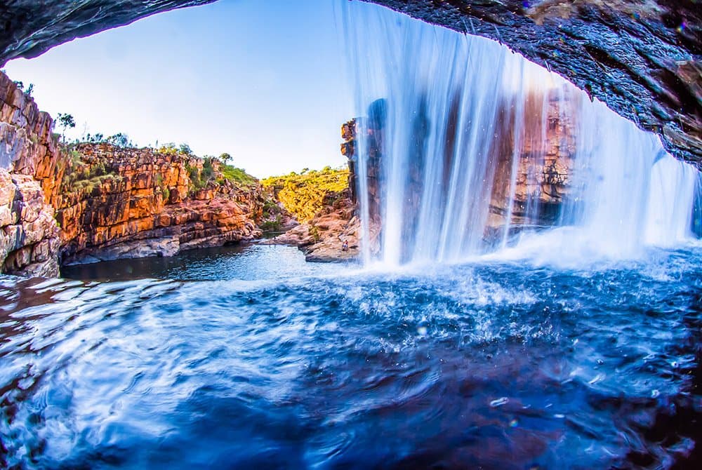 A waterfall and rocky Australian landscape viewed from behind a cave.